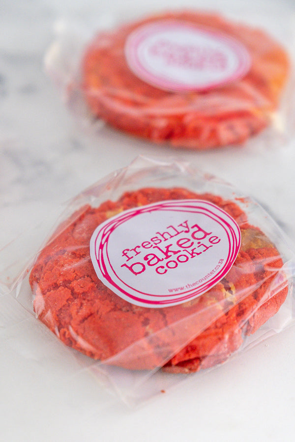 Two red velvet cookies in branded packaging