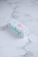 Load image into Gallery viewer, White fudge box with large, cursive turquoise text and colourful paint splashes around it; sitting on a white and grey marbled surface.
