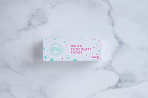 White chocolate fudge box with 'The Counter' logo in turquoise, surrounded by several thin lines creating a circle. Pink text stating 'white chocolate fudge' and paint splashes surrounding the text and logo.