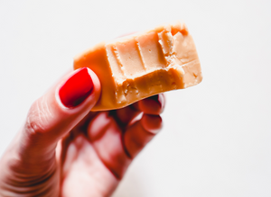 Hand with painted red nails holding a bitten block of white chocolate fudge