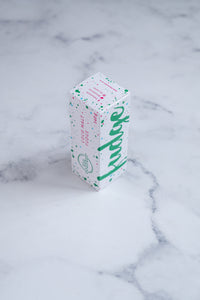 A white box stands upright on a neutral background. Large hunter green lettering states 'fudge' and is surrounded by hunter green and cerise pink paint splashes. The other side of the box that is visible has Paint splashes in hunter green and pink surround a messy circled logo for The Counter and the words 'Coco Malt fudge' are written in cerise pink block lettering. 