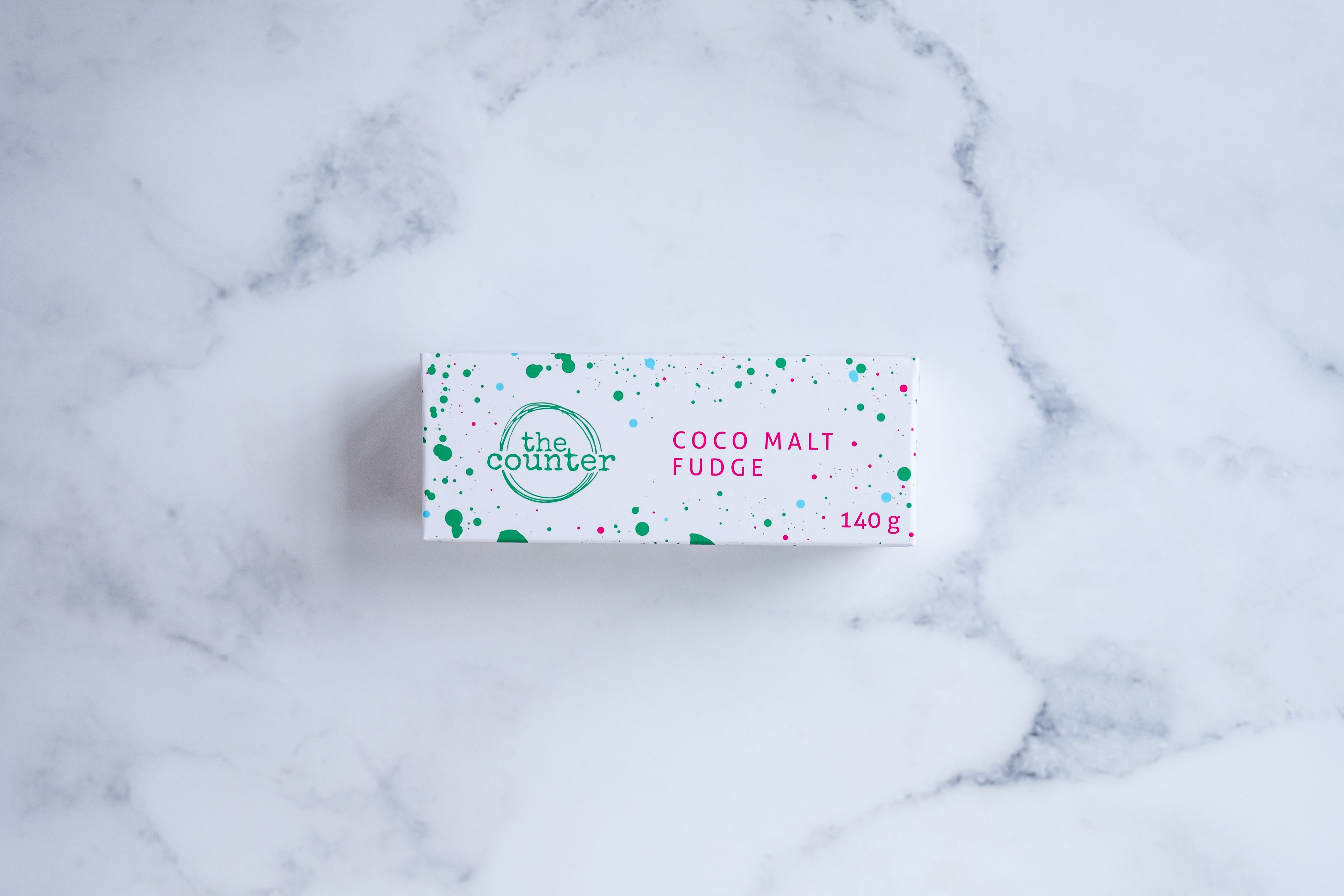 A white box sits on a neutral background. Large hunter green lettering states 'fudge' and is surrounded by hunter green and cerise pink paint splashes.