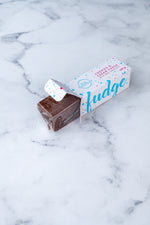 Load image into Gallery viewer, A large bar of dark chocolate and Oreo fudge (cookies and cream) peeks our from a white box. Paint splashes in bright blue and pink surround a messy circled logo for The Counter and the words &#39;Cookies &amp; Cream fudge with dark chocolate&#39; are written in cerise pink block lettering.
