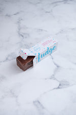 Load image into Gallery viewer, A large bar of dark chocolate and Oreo fudge (cookies and cream) peeks our from a white box. Paint splashes in bright blue and pink surround a messy circled logo for The Counter and the words &#39;Cookies &amp; Cream fudge with dark chocolate&#39; are written in cerise pink block lettering.
