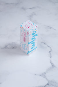 A white box stands upright on a neutral background. Large bright blue lettering states 'fudge' and is surrounded by bright blue and cerise pink paint splashes. A messy circled logo for The Counter and the words 'Cookies & Cream fudge with dark chocolate' are written in cerise pink block lettering.