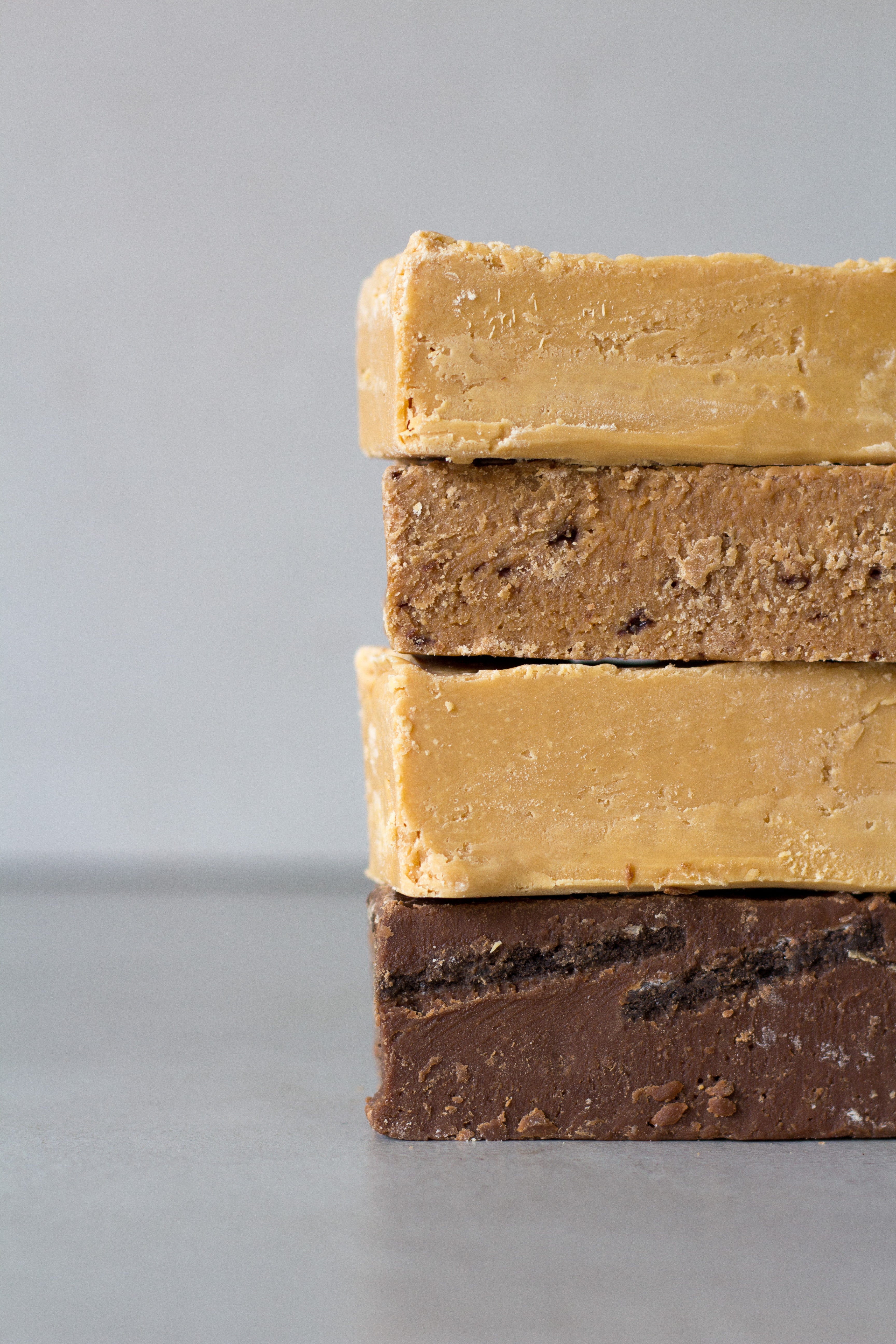 Four large blocks of fudge are stacked on top of each other, peeking out from the right side of the image - each in a different flavour and colour. The second block from the top is a slightly brown Coco Malt fudge bar.