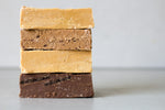 Load image into Gallery viewer, Four large blocks of fudge are stacked on top of each other - each in a different flavour and colour. The bottom fudge bar is a large dark chocolate bar, filled with Oreos.
