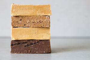 Four large blocks of fudge are stacked on top of each other - each in a different flavour and colour. The bottom fudge bar is a large dark chocolate bar, filled with Oreos.