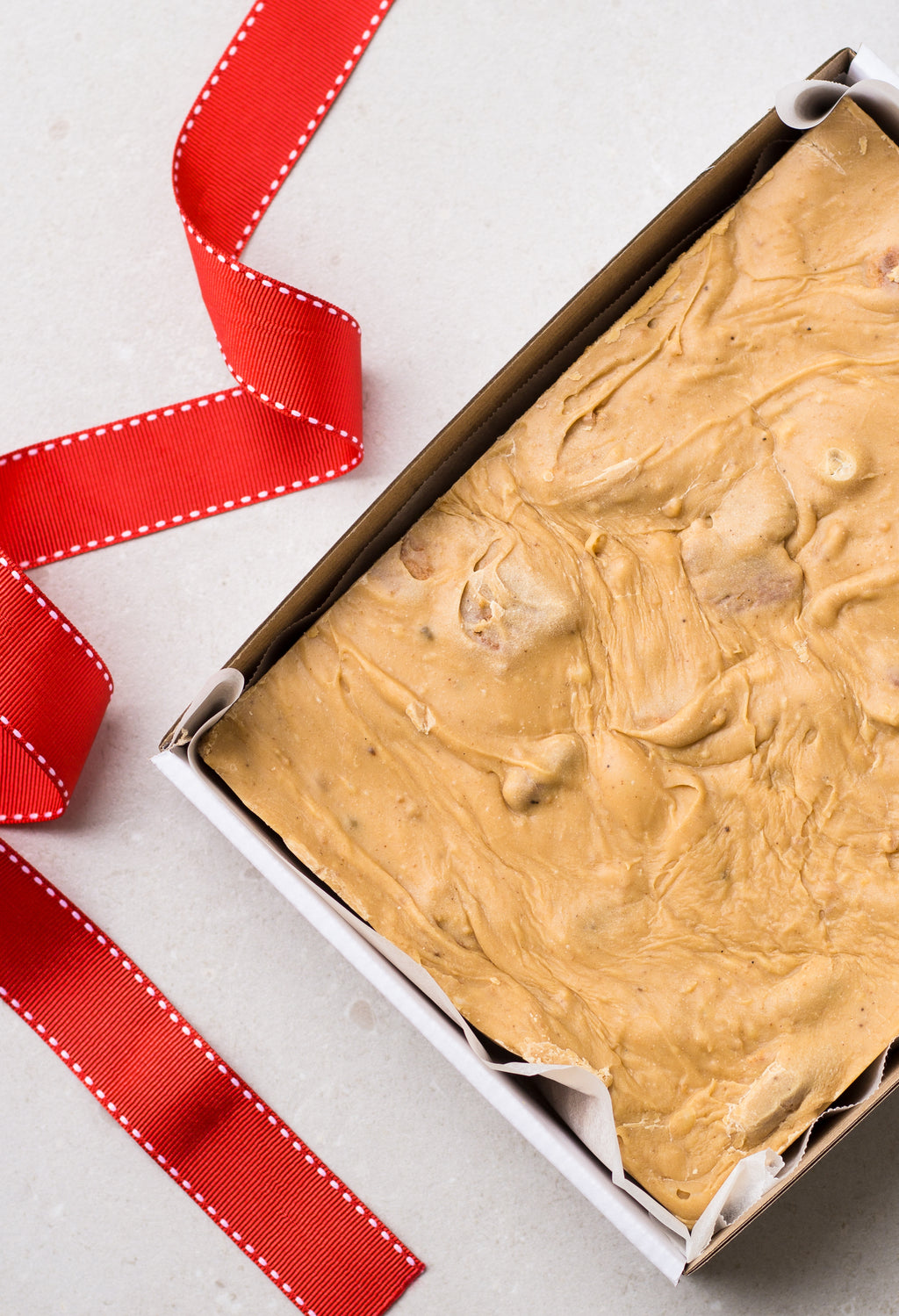 One kilogram slab of gingerbread fudge in a sturdy white cardboard tray - finished with a red saddle stitch ribbon.