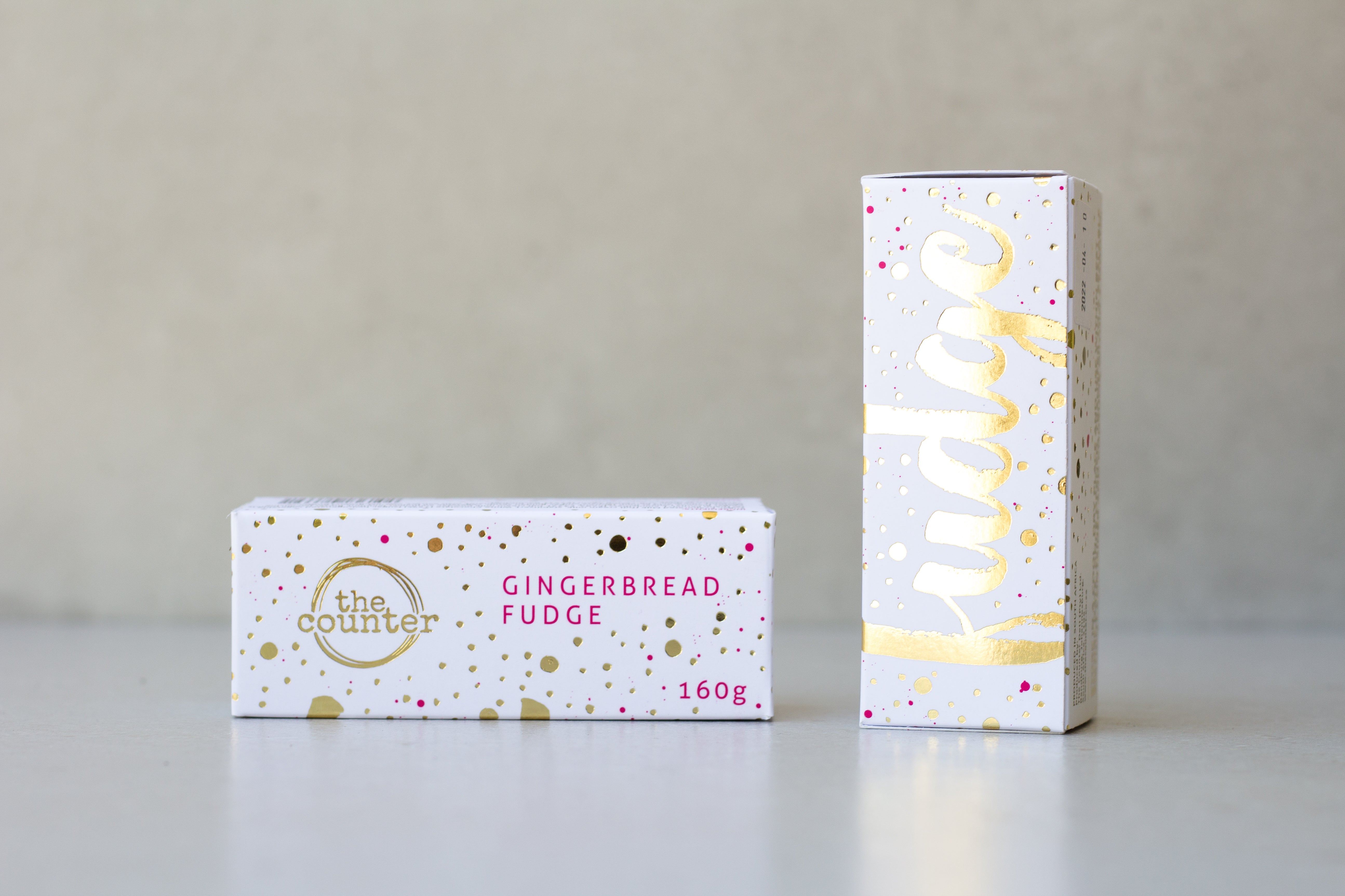 Gold foiled white box filled with gingerbread fudge. Two on a neutral surface - one upright.