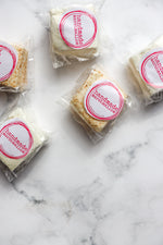 Load image into Gallery viewer, Packaged fluffy toasted coconut marshmallows with a pink and white label on a marble surface.
