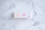 Load image into Gallery viewer, A white box sits on a neutral background. Paint splashes in orange and pink surround a messy circled logo for The Counter and the words ‘Peanut Butter Fudge&#39; are written in cerise pink block lettering.
