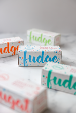 Load image into Gallery viewer, Five colourful fudge boxes sit on a marbled white surface, with the Cookies and Cream fudge box being the only one in focus. The box is white with bright blue large text stating &#39;fudge&#39; and a subtle logo and product description on the top of the box.
