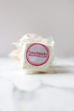 Load image into Gallery viewer, A handmade vanilla bean marshmallow with a label that reads 'handmade' on a marble surface.
