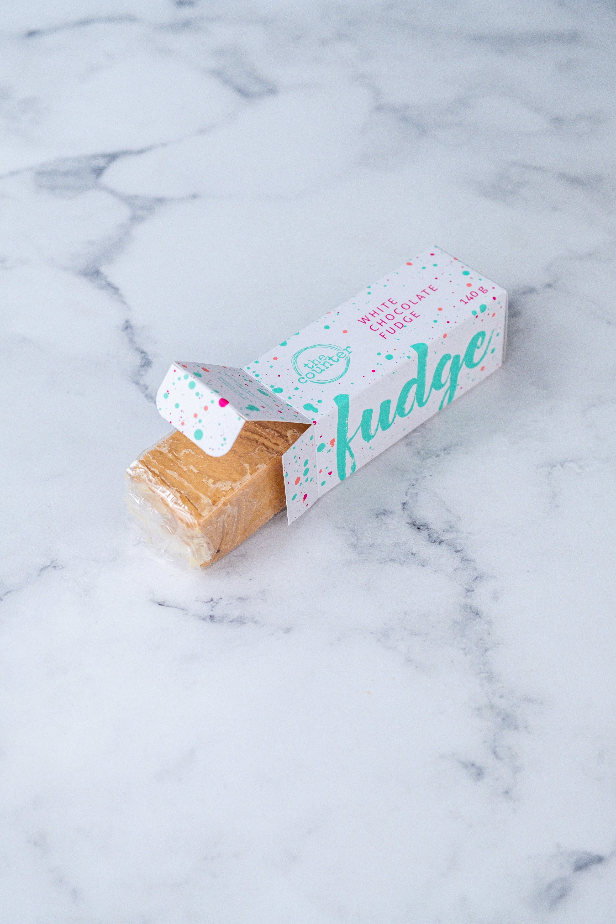 White chocolate fudge bar peeking out of a branded white, turquoise and cerise pink box.