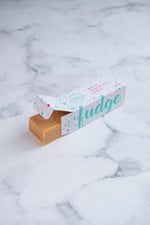 Load image into Gallery viewer, White chocolate fudge bar peeking out of a branded white, turquoise and cerise pink box.
