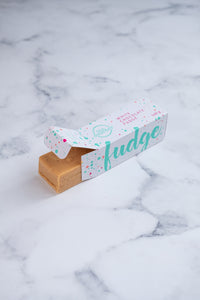 White chocolate fudge bar peeking out of a branded white, turquoise and cerise pink box.