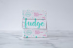 Load image into Gallery viewer, Three white fudge boxes with large, cursive turquoise text and colourful paint splashes around it; sitting on a white and grey marbled surface. Three boxes are stacked on top of each other; alternating between different sides of the box.
